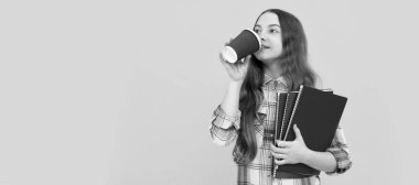 positive kid in checkered shirt with workbook drinking coffee from cup. Portrait of schoolgirl student, studio banner header. School child face, copyspace