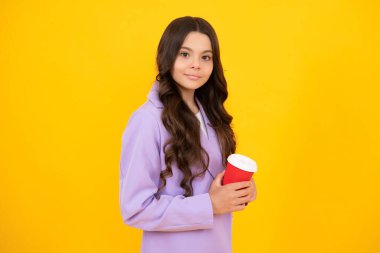 Child with coffee or tea cup isolated on yellow studio background. Teenage girl with take away beverage. Happy face, positive and smiling emotions of teenager girl