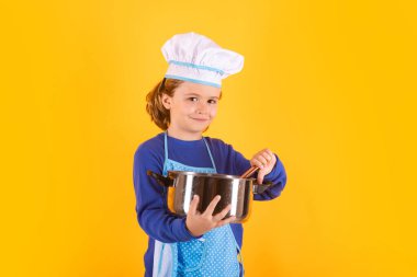 Çocuk tencere ve kepçeyle yemek pişiriyor. Çocuk aşçı, izole stüdyo geçmişinde yemek hazırlıyor. Çocuklar yemek yapıyor. Önlüğü ve aşçı şapkası olan genç çocuk sağlıklı bir yemek hazırlıyor.