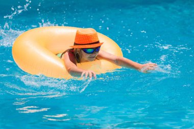 Child playing in swimming pool. Kids holidays and vacation concept. Summer kids cocktail. Happy little boy with inflatable ring in swimming pool