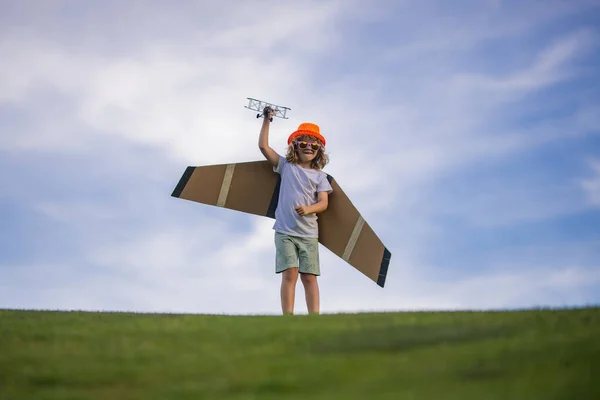 Little child boy is playing and dreaming of flying over the clouds. Pilot aviator child with a toy airplane plays on summer nature. Child playing with plane wings. Concept of dreams and travels