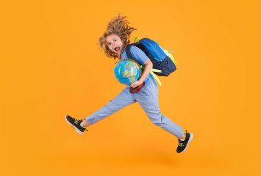Aptal çocuk okul çantası ve küreyle zıplıyor. Okul üniformalı, çantalı ve atlayan bir okul çocuğu. Stüdyoya atlayan okul çocukları izole edilmiş sarı arka plan