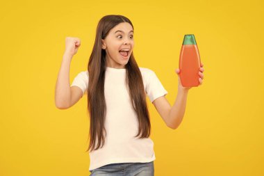 Teen child girl with shampoo bottle or shower gel isolated on yellow background. Kids hair cosmetic product. Excited teenager, glad amazed and overjoyed emotions