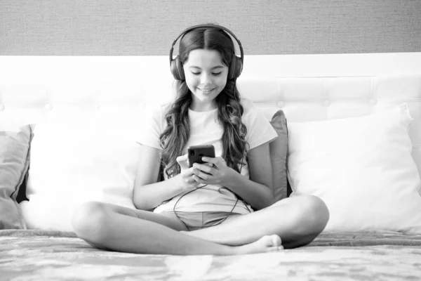 Glad Tonåring Flicka Bär Hörlurar Titta Videor Smartphone Sitter Sängen — Stockfoto