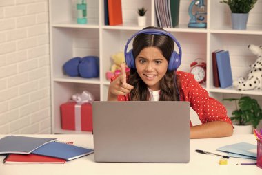 Masada oturan liseli kız ders çalışırken dizüstü bilgisayar kullanıyor. Mutlu kız yüzü, pozitif ve gülümseyen duygular. Heyecanlı bir yüz, neşeli genç bir kız.