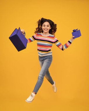 Sarı arka planda alışveriş torbaları olan güzel moda kızı. Alışveriş ve moda alışverişi. Koş ve atla. Alışveriş çantalı çocuk. Mutlu genç, pozitif gülümseyen duygular