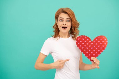 Mavi arka planda kırmızı kalbi olan genç bir kadın. işaret parmağı.