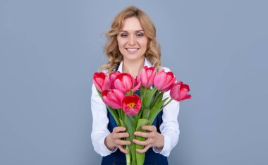 Gri arka planda bahar lale çiçekleri olan önlüklü neşeli genç bir kadın..