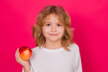Kid with apple in studio. Studio portrait of cute child hold apple isolated on red background