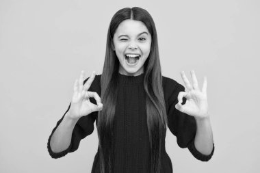 Küçük bir kızın portresi iyi bir hareket gösteriyor ve sarı arka planda izole edilmiş bir şekilde göz kırpıyor. Tamam imza konsepti. Heyecanlı bir yüz. Şaşırtıcı bir ifade, neşeli ve mutlu.