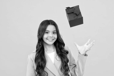 Happy teenage girl. Teenager child holding gift box on isolated yellow background. Gift for kids birthday. Christmas or New Year present box. Smiling kids emotions