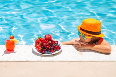 Çocuk yaz tatilinde yüzme havuzunun yanında meyve yiyor. Çocuklar dışarıda meyve yer. Çocuklar için sağlıklı meyveler