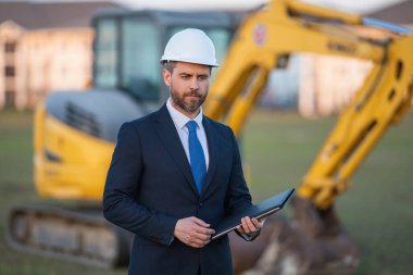 Kazıcının yanında inşaat işçisi. Evin önünde kendine güvenen bir inşaat sahibi. Mimar, inşaat mühendisi. İnşaat alanında güvenlik yeleği ve kasketi olan bir inşaat sahibi.