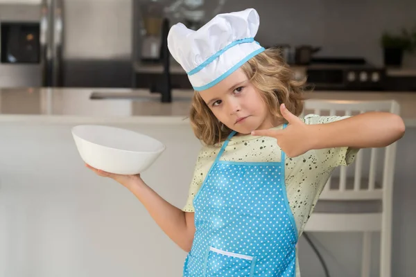Aşçı çocuk ev mutfağında yemek pişiriyor. Aşçı çocuk mutfakta aşçılık yapıyor. Yemek pişirme, aşçılık ve çocuklar. Aşçı şapkalı ve önlüklü küçük çocuk.