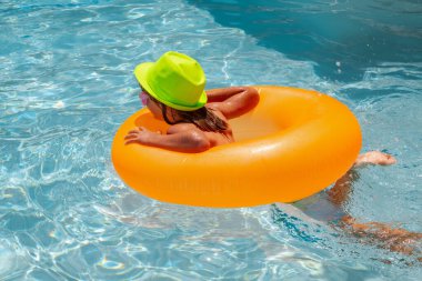 Çocuklar yüzme havuzunda yüzer. Çocuklar tatil ve tatil konsepti. Yüzme havuzunda turuncu şişme yüzüklü mutlu küçük çocuk.