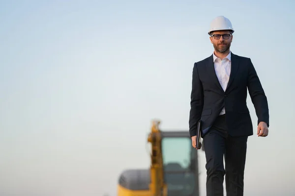 stock image Construction owner near excavator. Confident construction owner in front of house. Architect, civil engineer. Man construction owner with a safety vest and hardhat at construction site