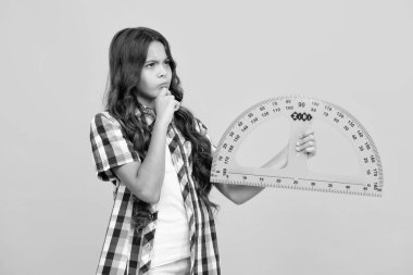 Okul kızı geometri dersi için ölçü tutuyor, sarı arka planda izole edilmiş. Ölçüm aletleri. Öğrenci matematiği okuyor. Düşünen zeki liseli kız