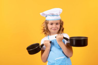 Aşçı çocuk tencereyle yemek pişiriyor. Çocuk pişirme, küçük şef yemek hazırlıyor. Sarı stüdyodaki aşçı şapkalı ve önlüklü çocuk izole edilmiş.
