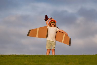 Kid pilot aviator with with paper wings dreams of traveling in summer in park outdoor