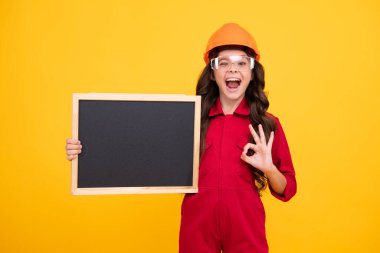 Kask takmış ergen bir çocuk. Kasklı çocuk. Çocuk mühendis inşaat alanında. Yenileme ve onarım. Heyecanlı genç kız fotokopi için tahtayı tutuyor