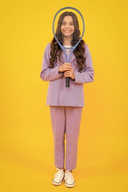 Genç tenisçi kız izole edilmiş sarı arka planda tenis raketi tutuyor. Çocuklar için spor. Küçük çocuk için antrenman. Çocuk tenis oynamayı öğreniyor