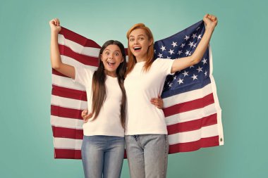 Heyecanlı anne ve çocuk Amerikan bayrağı taşıyor. Vatansever bayram. Mutlu aile, mavi izole edilmiş stüdyo geçmişinde Amerikan bayrağı taşıyan anne ve kızı. ABD 4 Temmuz 'da bağımsızlığını kutladı
