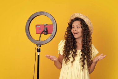 Genç blog yazarı etkileyicisi çevrimiçi video dersi yapmak için tripoda selfie kaplı lamba ve akıllı telefon kullanıyor. Genç vlogger çocuk kanalı için video blogu yapıyor. Genç bir kızın pozitif ve gülümseyen duyguları