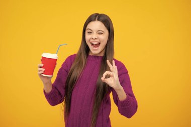 12, 13, 14 yaşlarında çocuk elinde bir fincan kapuçino ya da çay ile. Sarı arka planda yemek kupası olan çocuk, sabah içeceği. Heyecanlı bir yüz. Şaşırtıcı bir ifade, neşeli ve mutlu.