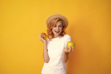 Elma tutan genç bir kadın mutlu ve havalı bir gülümsemeyle gülümsüyor, dişlerini gösteriyor. Sarı arka planda, elinde elma tutan mutlu ve güzel bir kadın görüntüsü.