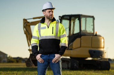 İnşaat işçisi endüstriyel alanda kazıcı ile çalışıyor. Kask takan, buldozerli bir işçi. Mühendis, inşaat firmasında çalışıyor. Traktörlü kazı ustabaşı