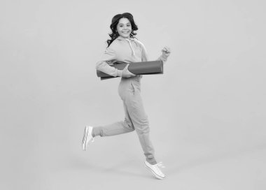 Run and jump. Teen girl 12, 13, 14 years old in sport suit. Fashion child in sportswear sportive clothing. Sportive fashionable outfit. Studio shot on yellow background