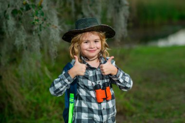 Yaz tatili. Dürbünlü çocuk doğa yürüyüşü yapıyor. Küçük kaşif. Çocuklarla açık hava eğlencesi ve maceralar. Güneşli kırsal kesimde çocuk turist