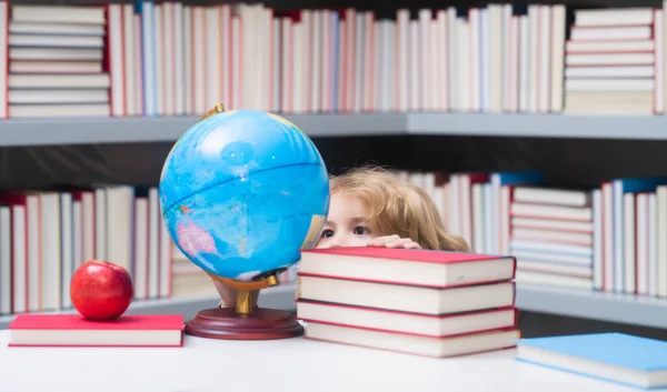 School boy looking at globe in library, geography lesson. School child student learning in class, study english language at school. Elementary school child. Portrait of funny pupil learning