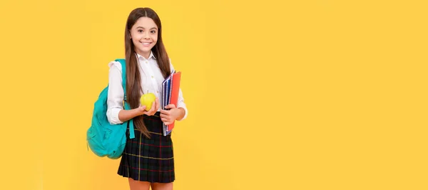 stock image smiling teen girl with backpack and workbooks hold apple lunch in uniform full length, school lunch. Banner of schoolgirl student. School child pupil portrait with copy space