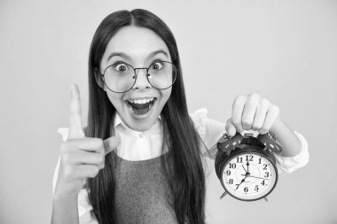 Portrait of teenage girl with clock alrm, time and deadline. Studio shot isolated on yellow background. Surprised teenager girl