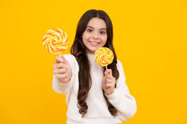 Genç kız sarı arka planda lolipop karamel tutuyor, şekerci dükkanı. Tatlılı ergen enayiler. Mutlu yüz, pozitif ve gülümseyen genç kız duyguları