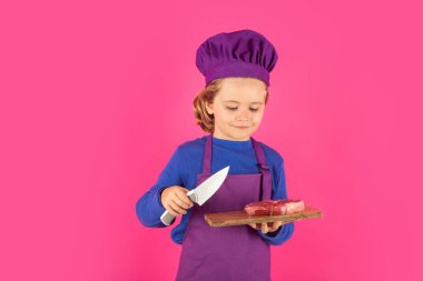 Çocuk aşçı et bifteği ve bıçakla kesme tahtasını tutuyor. Aşçılık, aşçılık ve çocuk maması konsepti.