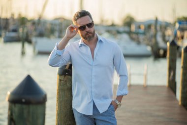 40 'lı yılların adamı yatın yanında. Dışarıdaki mankenin portresi. Moda erkeği yatların yanında poz veriyor. Şehir tarzında bir moda adamı. Yat kulübündeki yakışıklı İspanyol adam. Lüks yatın yanındaki körfezdeki adam.