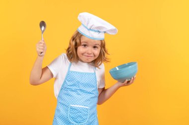 Kid chef cook with cooking bowl. Kid in cooker uniform and chef hat preparing food on studio color background. Cooking, culinary and kids food concept