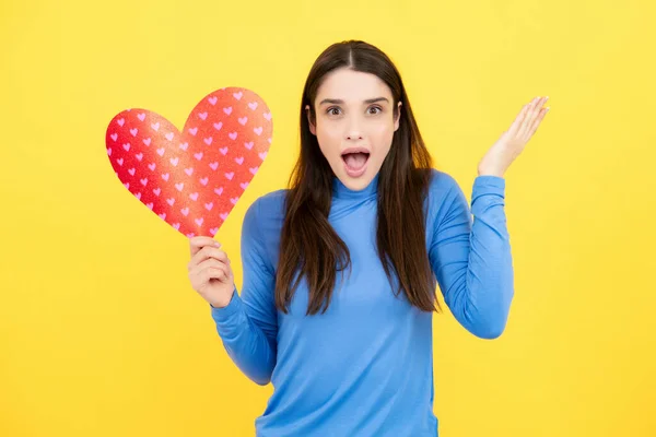 Stock image Valentines Day. Beautiful young woman with heart in her hands. Attractive woman with paper heart over yellow background