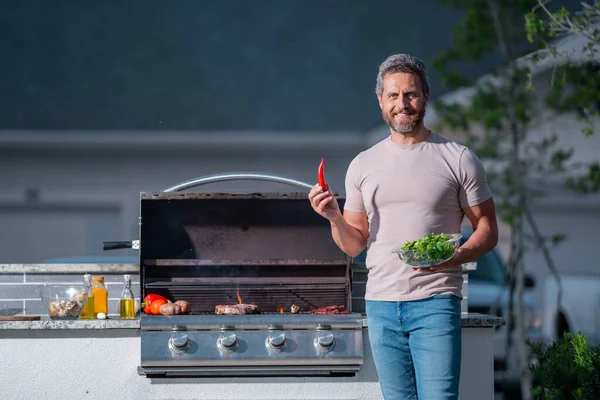 stock image Man cooking meat on barbecue in the backyard of the house. Handsome man preparing barbecue. Barbecue chef master. Man in apron preparing delicious grilled barbecue food, bbq meat. Grill and barbeque