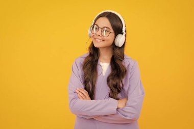 Teenager child girl in headphones listening music, wearing stylish casual outfit isolated over yellow background