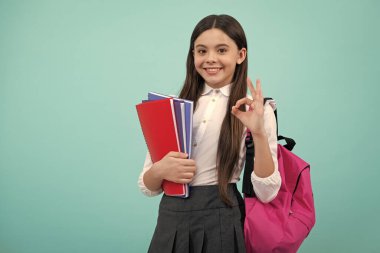 Okul çantalı genç kız mavi izole stüdyo geçmişi üzerine kitap tutuyor. Çocuk okulu ve eğitim konsepti