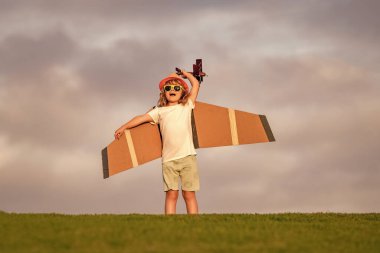 Kid pilot aviator with with paper wings dreams of traveling in summer in park outdoor