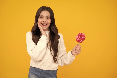 Genç kız sarı arka planda lolipop karamel tutuyor, şekerci dükkanı. Tatlılı ergen enayiler. Mutlu yüz, pozitif ve gülümseyen genç kız duyguları
