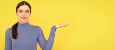 Sarı arka planda bayan portresi. Reklam. Ürün sunan kadın. İzole edilmiş yüz portresi, afiş başlığı posteri ve kopyalanmış kopya alanı