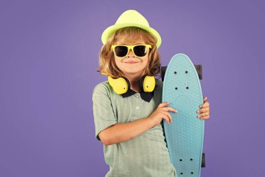 Happy child boy holding skateboard over blue background isolated. Studio portrait of fashion kids