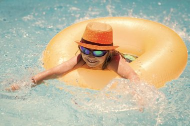 Child playing in swimming pool. Kids holidays and vacation concept. Summer kids cocktail. Happy little boy with inflatable ring in swimming pool