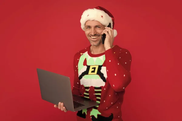 電話カードとラップトップでサンタ クリスマスセーターの男と色の背景の帽子 中世のサンタ — ストック写真