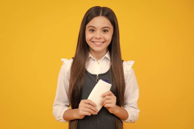 Sarı arka planda şampuan şişesi ya da duş jeli olan genç bir kız çocuğu. Çocukların saçı kozmetik ürün